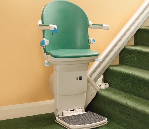 A stairlift installed on the side of a staircase, featuring a folded footrest and a green chair.