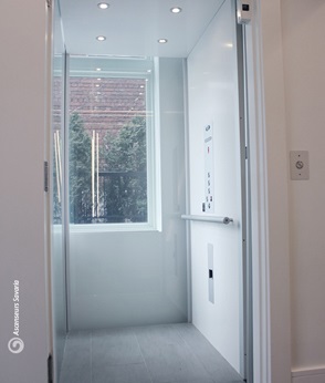 Modern residential elevator with glass doors and a view of a brick building outside.