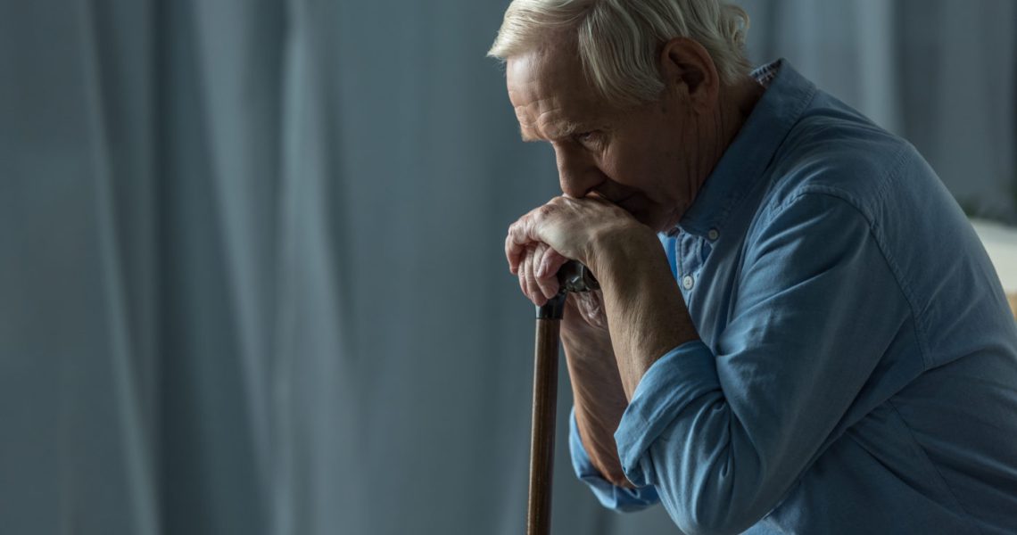 Elderly man resting on a cane, appearing contemplative or tired.