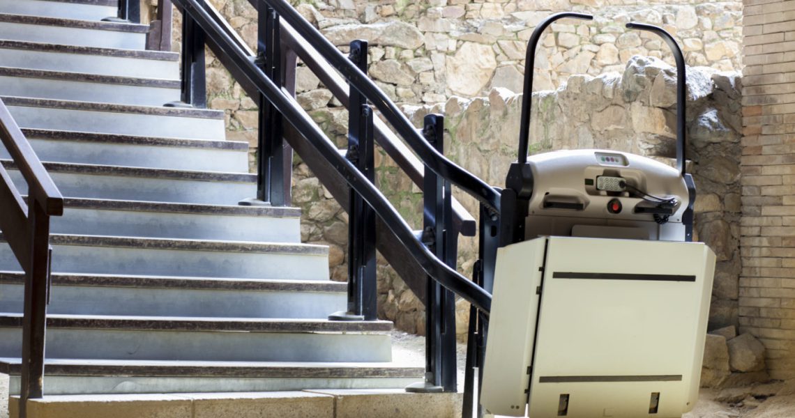 Wheelchair stair lift installed next to a staircase at an outdoor location.