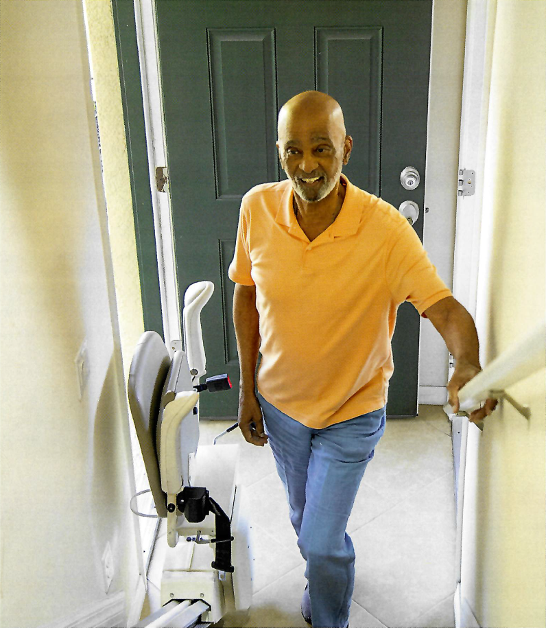 A smiling man standing by a stairlift inside a home.