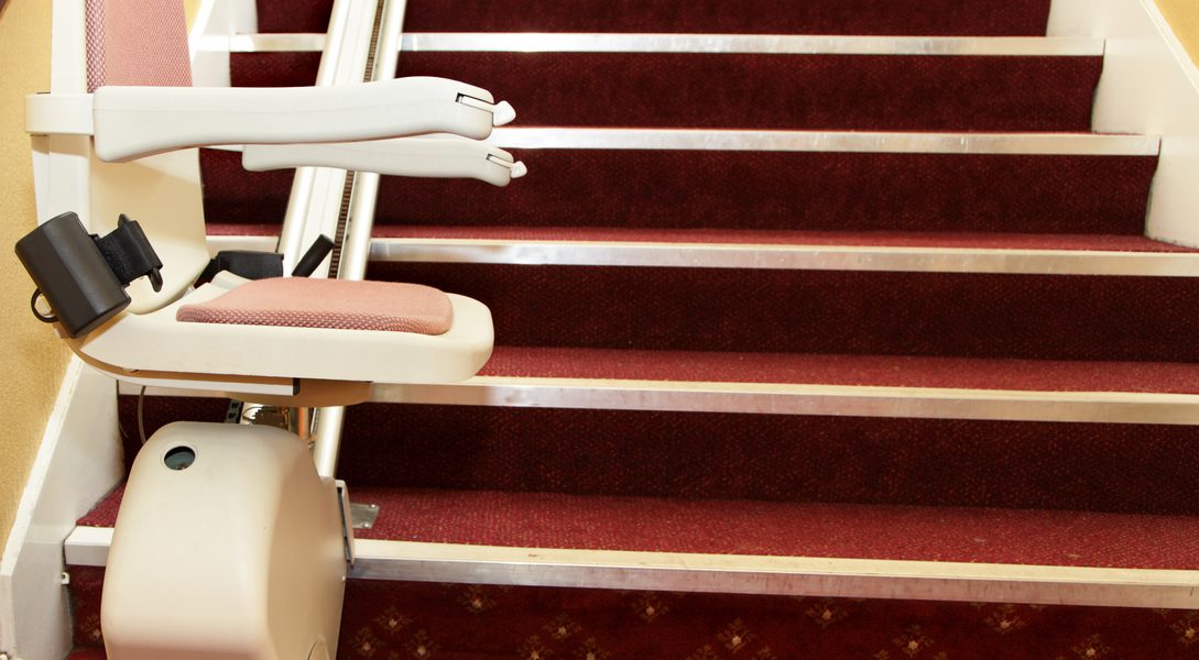 A stairlift installed on a staircase with red carpeting.