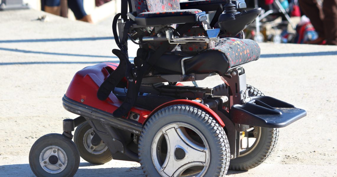 Red and black motorized wheelchair on a gravel surface.