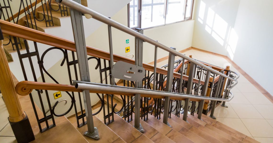 An interior view of a modern staircase with wooden steps, metal railings, and accessibility signs.