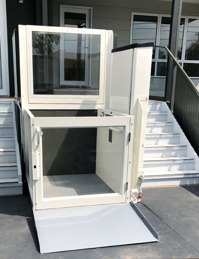 An open vertical platform wheelchair lift installed at the entrance of a building.